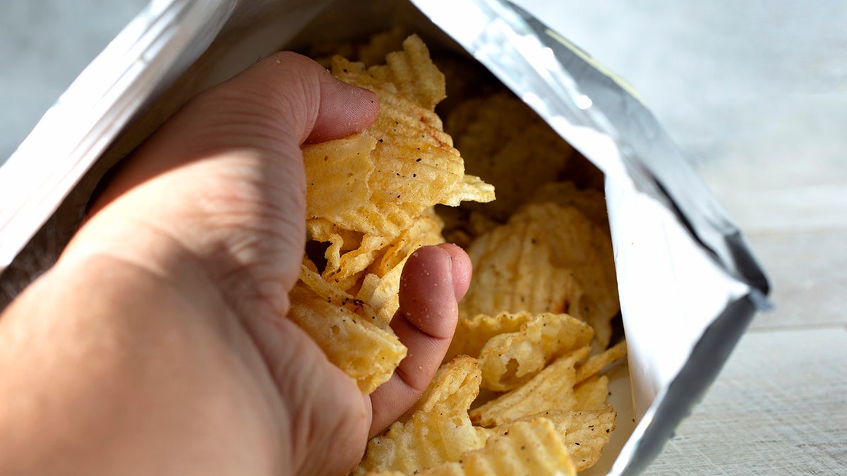 A view of a hand that draws a good handful of fries from a product bag.